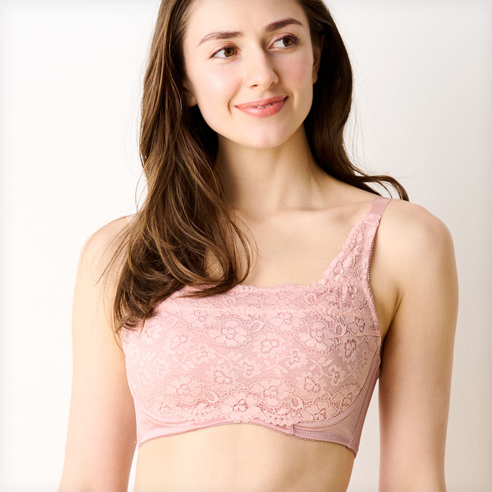 ベビーピンクの胸を小さく見せるブラ、メイン商品画像。レース素材のブラを着用した女性モデルが微笑む正面写真。快適な着心地とエレガントなデザインを強調